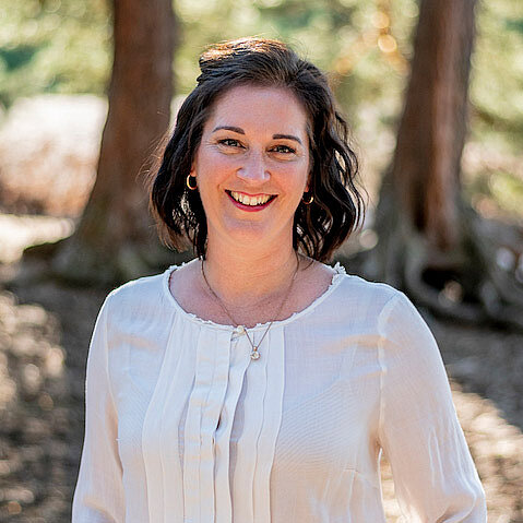Katrin Kaiser in a white blouse in front of 3 trees that can be seen blurred in the background