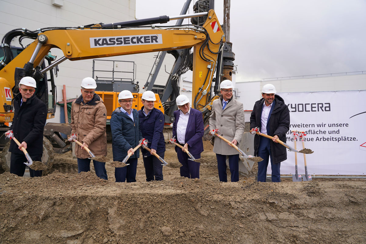 Ground-breaking ceremony by 7 people with helmets and shovels in front of an excavator